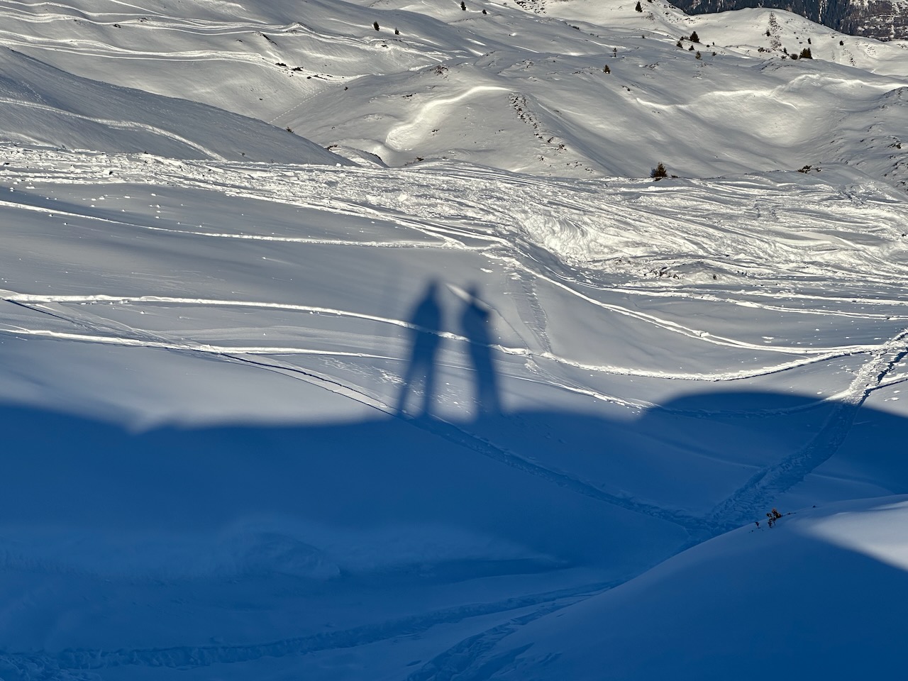 A snowy mountainous landscape showing the shadows of two figures